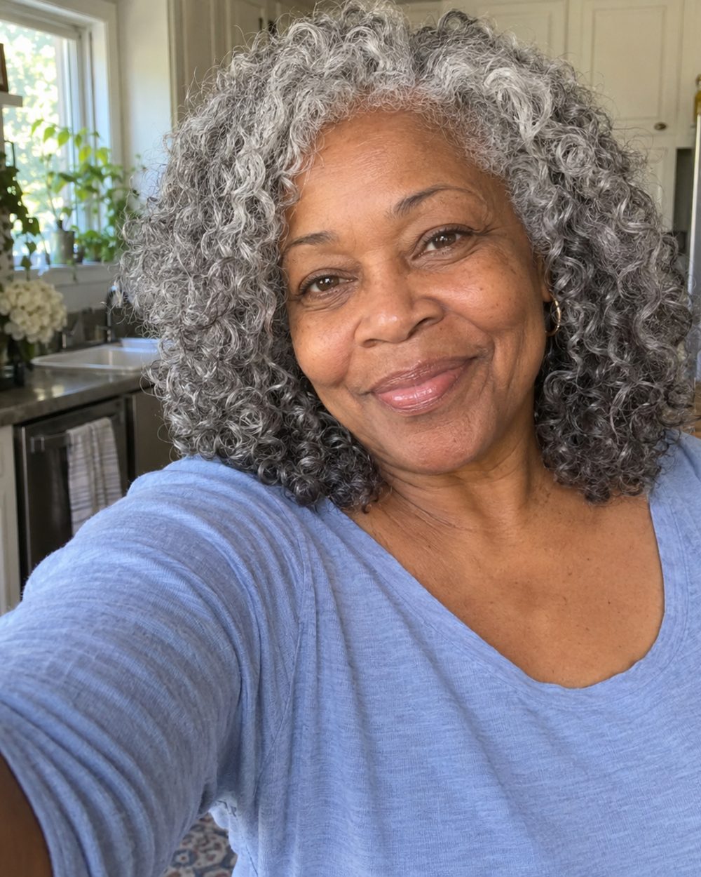 A woman with full, voluminous grey curls smiling in her kitchen.