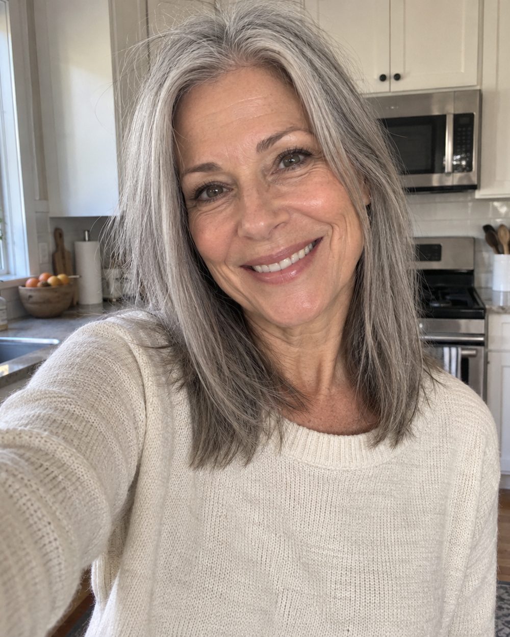 A woman with long, thick silver hair smiling in her kitchen.