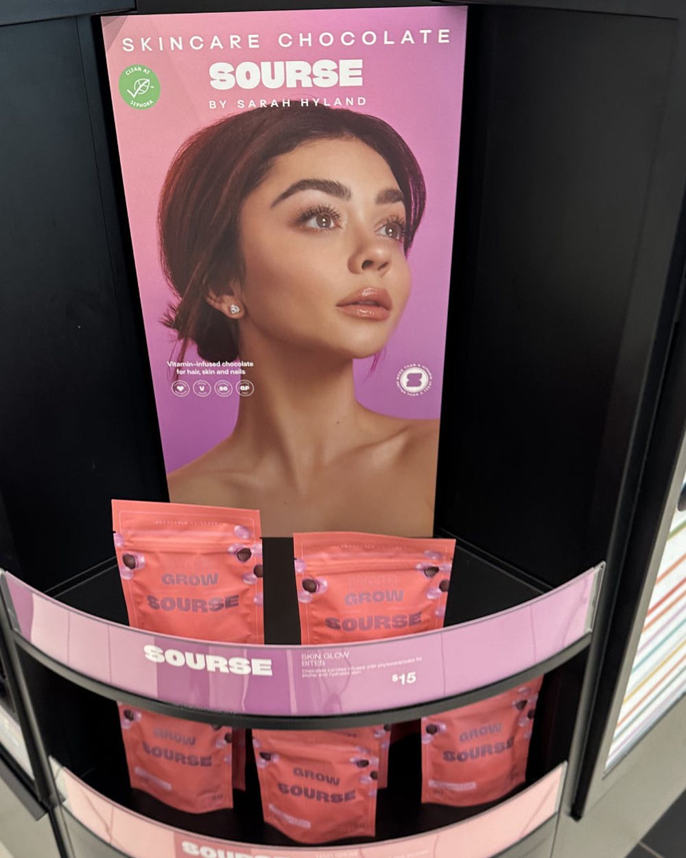 Sourse Hair Grow Bites pouches on a Sephora store display beneath a Sarah Hyland poster.